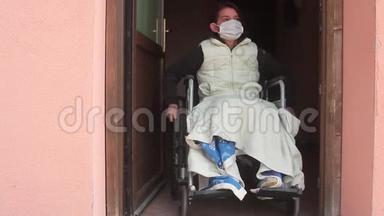 残疾妇女独自一人坐在轮椅上，戴着防护面罩，望着外面的敞开的房门，呆在家里进行检疫