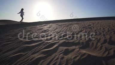 日落时分，沙漠中一个美丽的女孩沿着沙丘散步的剪影。 西班牙大加那利马斯帕洛马斯沙漠