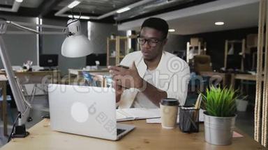 非洲商人正在用笔记本电脑工作，并在现代办公室接听电话