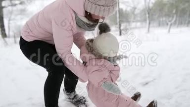 母亲在雪地里养育孩子. 穿暖和连衣裙的孩子学会走路。 在冬天森林里走第一步的女孩