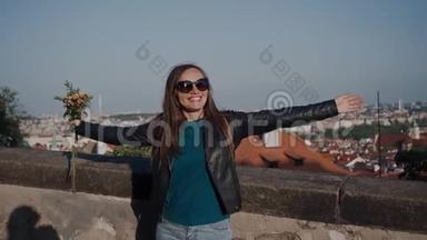 戴墨镜和皮夹克的微笑女孩站在有手臂的房子屋顶的石墙附近
