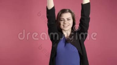 年轻女子微笑着在粉红背景下在演播室跳舞。