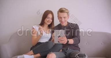 一对年轻可爱的白种人夫妇在平板电脑上打了个视频电话，他们坐在平板电脑上挥手。