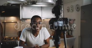 快乐年轻聪明的黑色博客男子拍摄新的<strong>vlog</strong>视频与专业相机在厨房在家慢动作。