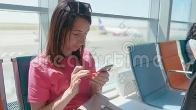 一个年轻漂亮的女孩坐在机场候车室，用<strong>手机</strong>。 女人买<strong>电子</strong>机票，做酒店
