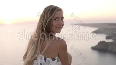 一个头发<strong>长长</strong>的金发女郎正坐在海边的岩石上，欣赏着日落，望着那边