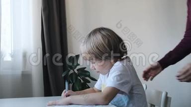 小男孩，孩子，坐在家里的桌子旁画画，妈妈亲吻拥抱他