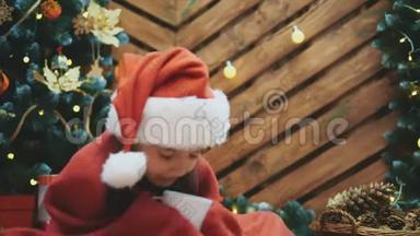圣诞老人帽子里睡意朦胧的孩子的特写<strong>视频</strong>，<strong>圣诞树</strong>旁裹着红毯，端着一杯可可，看着