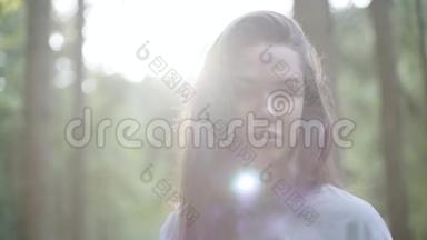 美丽的女人在绿色的森林里站在阳光下看着远方的肖像。 那个女孩在森林里徒步旅行