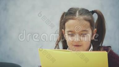 一个勤奋的小女生坐在桌边看书。灰色背景。