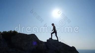 自信的年轻女子在日出时缓慢地走向山顶。 一位<strong>女士</strong>徒步旅行的<strong>剪影</strong>