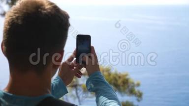 无法辨认的人在他的智能手机上拍摄风景迷人的海景。 年轻人用手机拍漂亮的照片