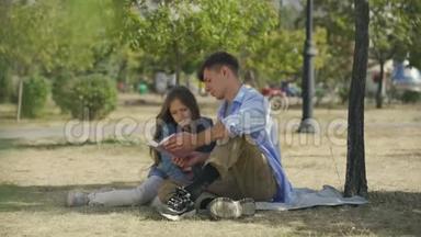 一个十几岁的男孩和他的小妹妹一起读诗歌或故事书，在阳光明媚的公园里坐在户外讨论