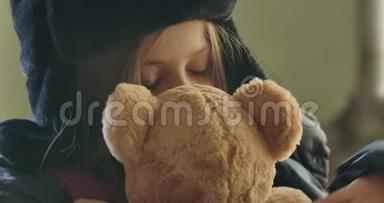 一个可爱的无家可归的女孩戴着帽子，带着耳机拥抱泰迪熊的特写肖像。 绝望的<strong>难民</strong>等待帮助。