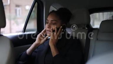 一位漂亮的美国黑人女商人坐在出租车后座上，坐在一个带着明亮皮革沙龙的出租车上，在她的移动电话旁交谈