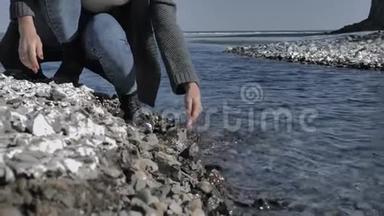 年轻的女孩滋润她的手，蘸着清澈的水在岩石海岸，阳光明媚的一天
