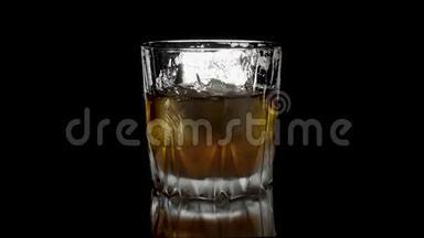冰块在一杯威士忌中旋转融化。 孤立在黑色背景上。 在白色威士忌中旋转冰块