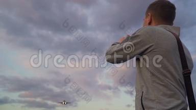 青年拍飞机在傍晚云天飞行的照片。 使用智能手机