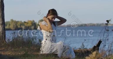 迷人的白种人女人坐在湖岸上，在<strong>闷热</strong>的夏日，触摸她的头发。 美丽的女孩