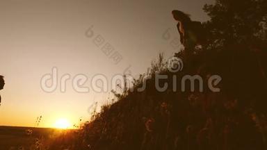 一个女旅行者向一个男人伸出手，在夕阳下爬上山顶。 旅行者手牵着手爬上悬崖