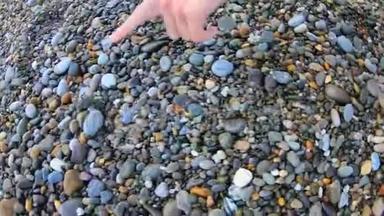 年轻女子试图用手指触摸小螃蟹跑在鹅卵石海滩上看水。 操作摄像机视图。