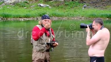 渔夫和摄影师站在河里。 一位留着长发和圣诞老人胡须的老人选择了一个捕蝇鱼饵