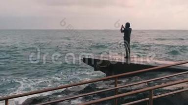 小男孩给暴风雨的大海<strong>拍照</strong>。 站在码头<strong>拍照</strong>的人。 孤独的男孩拍摄风洋的视频。 侧视图y