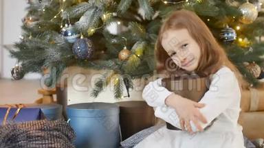 微笑着<strong>可爱</strong>的金发女孩拥抱着一个金色的<strong>礼盒</strong>，她坐在圣诞树旁，快乐的童年和圣诞节