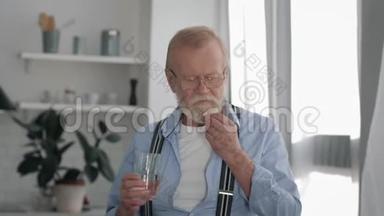 健康和护理，戴眼镜的病高年级男子，在白色房间里吃药，喝<strong>玻璃水</strong>