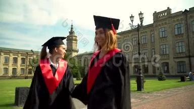 两个快乐的女孩在壁炉里走向大学大楼。 年轻人庆祝他们的毕业典礼