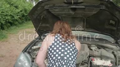 后面的女孩穿着有斑点的衣服，靠近汽车，带着打开的引擎盖。 女孩笑着满意地转过身来，擦着额头