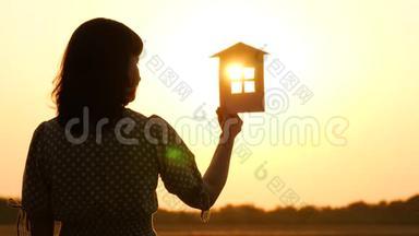 日落时分一个女孩的剪影，她带着一个模特回家。 太阳`光线穿过纸房的窗户。 这就是