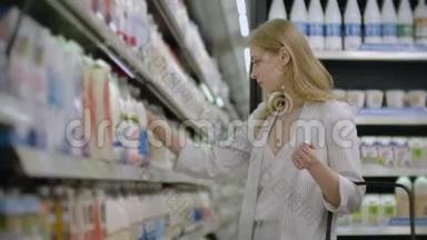 一个女人从超市冰箱里拿了一瓶牛奶，读了产品的标签和成分。 喂奶