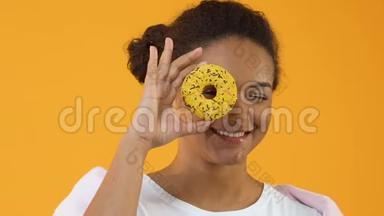 微笑的女时髦手拿着黄色的甜甜圈，甜点，零食