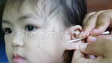 一位母亲用棉签`她的手清洁了小亚洲女孩`耳道