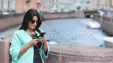 可爱的时尚女孩用智能手机从历史城市景观堤拍照