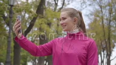 身着粉色运动服、面带微笑的白人女运动员通过视频聊天聊天和竖起大拇指的照片。开朗的