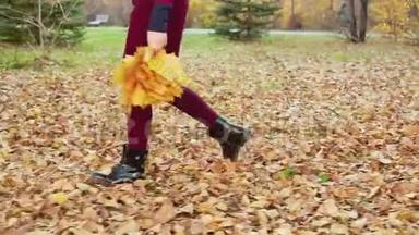 秋天公园里，腿上的少年女孩在落叶上散步。 走着的少年女孩踢着秋天的城市里的橙色树叶
