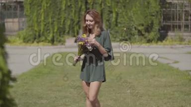 一幅美丽的年轻女子穿着<strong>短裙</strong>，站在夏日公园里嗅着一束野花的肖像