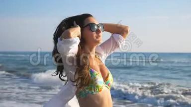 美丽的黑发美女戴着太阳镜沿着海洋海岸奔跑，享受自由。 有魅力的女人在玩的画像