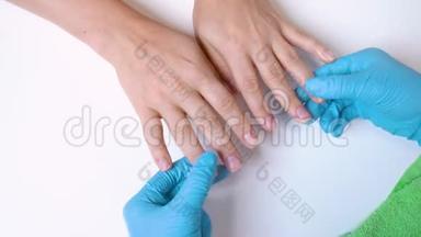 在手套中处理指甲的客户€™的手和指甲大师的特写，用奶油按摩和<strong>滋润</strong>指甲，