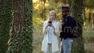 以自然为背景的秋装时装肖像。 在户外使用智能手机的情侣。 无忧无虑的秋日情侣