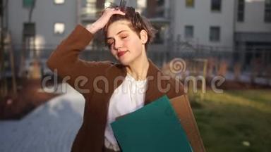 一个穿棕色外套的短发女孩手里拿着一个文件夹。 一的女商人在一个院子里