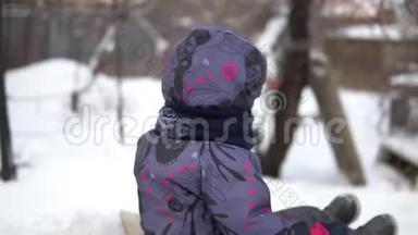 一个孩子在雪<strong>地滑</strong>梯上翻滚。 冬天在街上玩。 在寒冷的冬天，孩子穿着一件夹克和一件