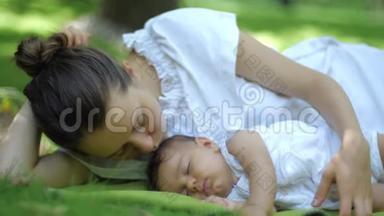 妈妈吻她的孩子睡在<strong>绿草</strong>的户外。 <strong>绿</strong>色<strong>夏日</strong>公园里微笑的年轻母亲和孩子