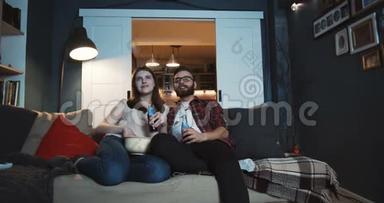 快乐的年轻白种人浪漫的学生夫妇一起在家看电影，用投影仪慢动作喝饮料。