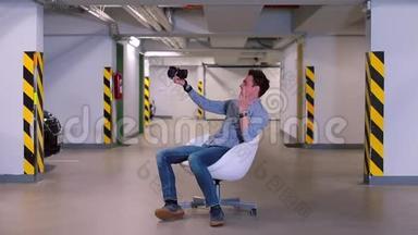 一个男人坐在<strong>地下车库</strong>里的扶手椅里，手里拿着相机。