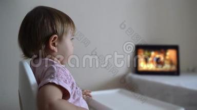 婴儿学步的女孩坐在高椅上，在平板电脑上看动画片。 <strong>新一代</strong>
