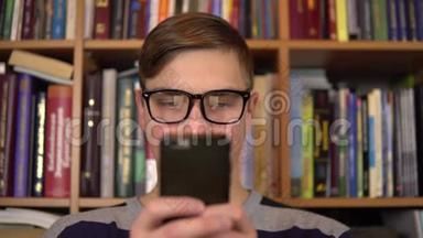 一个年轻人正在图书馆里看智能手机。 戴眼镜的人仔细地看着手机特写。 在里面