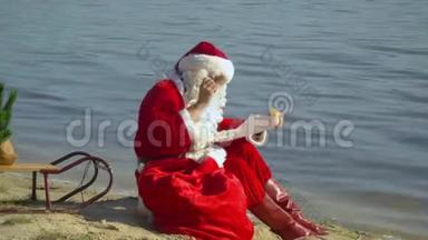 圣诞老人坐在湖边的沙滩上，拿着一袋礼物，在他的礼物清单上反思。 度假村的圣诞老人
